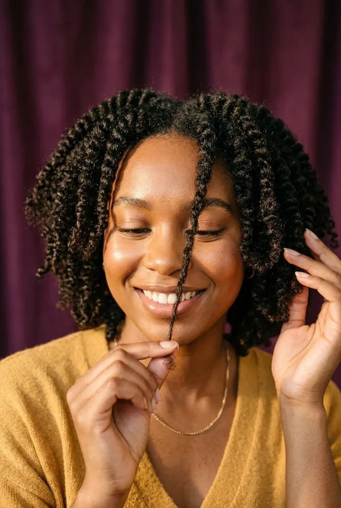 Femme afro souriante qui mesure une mèche de ses cheveux crépus naturels entre ses doigts